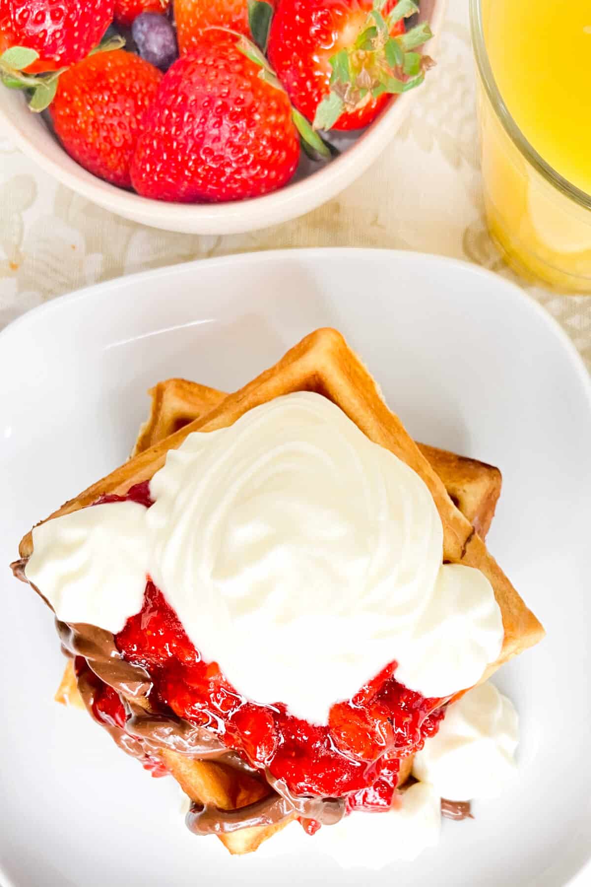 Waffles topped with nutella, strawberries, and whipped cream.