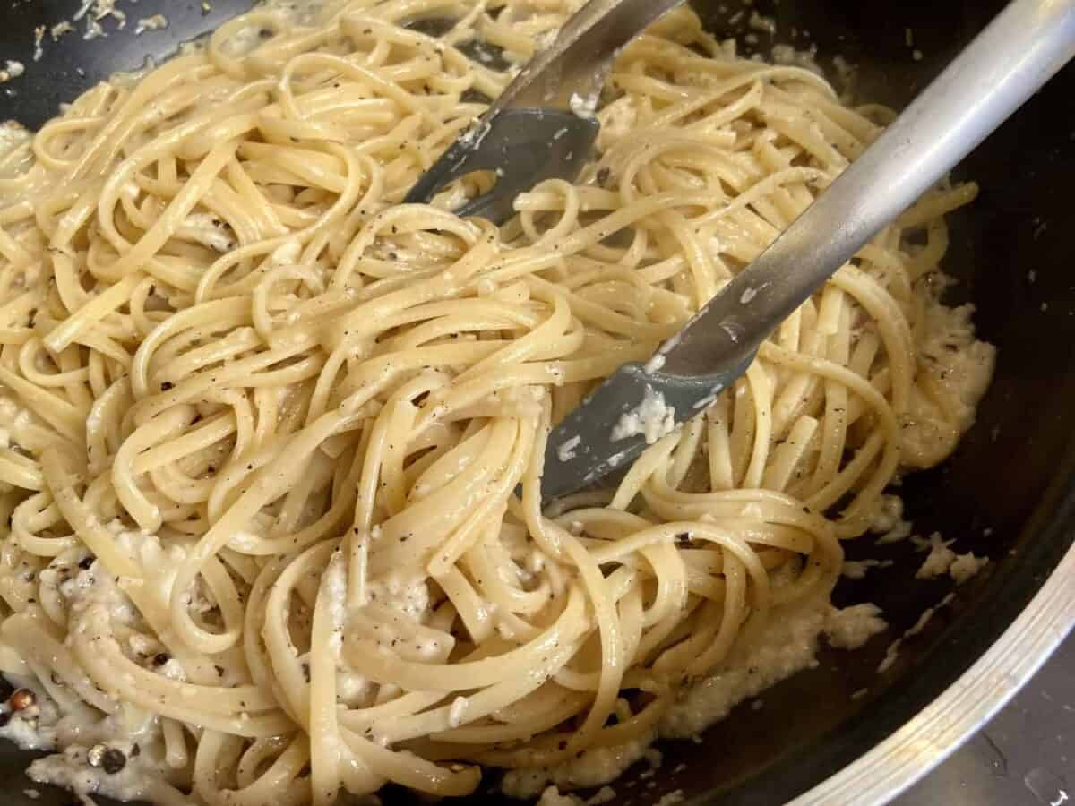 Tossing pasta in pan with tongs.