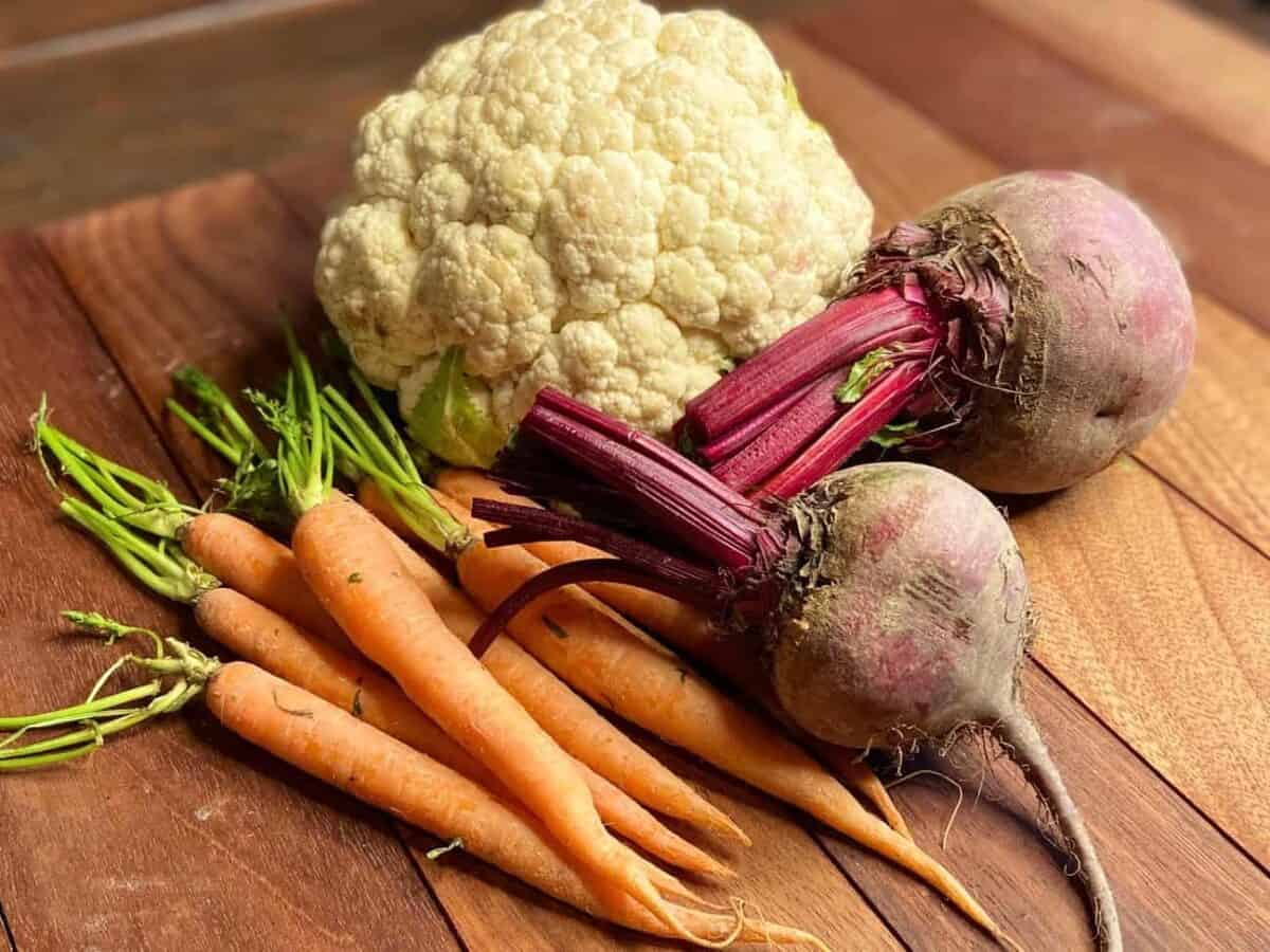 Carrots, cauliflower, and beets on a chopping board.