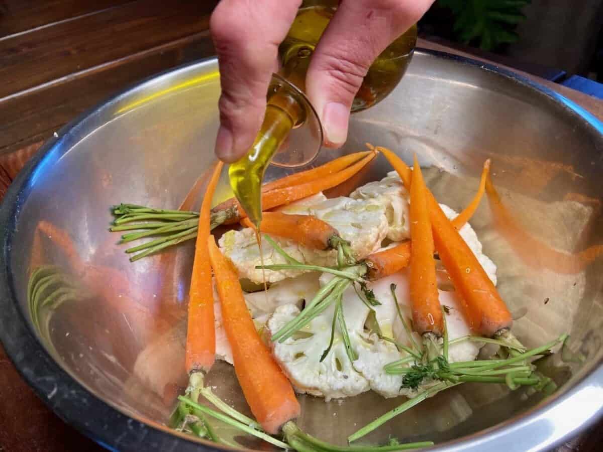 Sprinkling olive oil over vegetables in bowl.