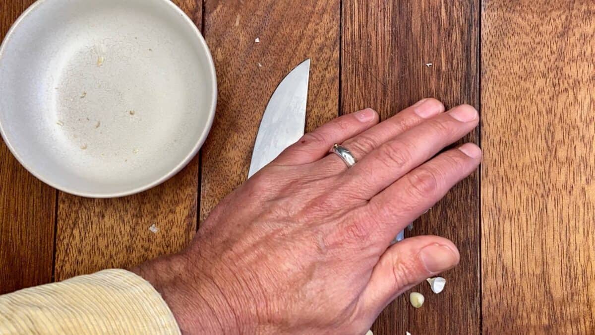 Applying gentle pressure with a knife to the garlic clove.