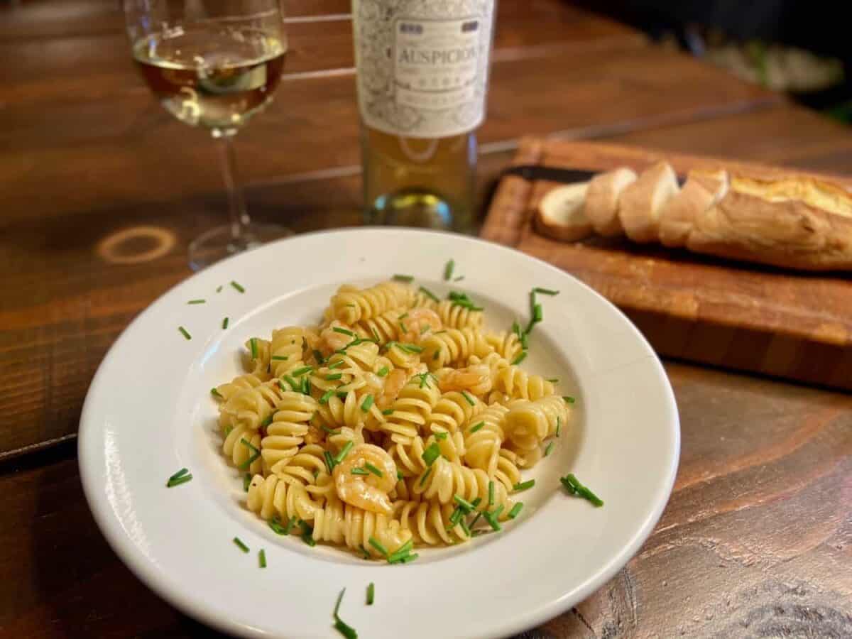 Served in a white pasta bowl, with a bottle of wine, wine glass, and baguette.