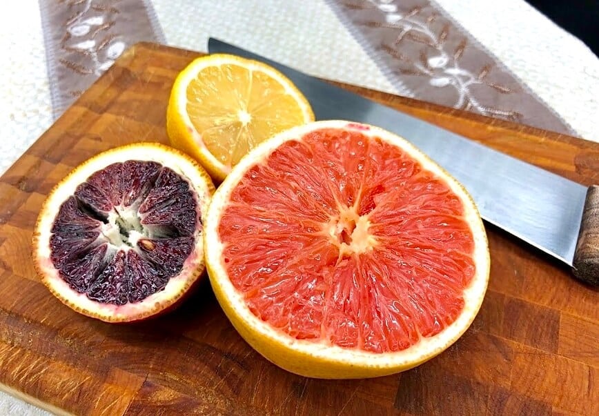 Lemon, blood orange, and grapefruit on a wooden cutting board.