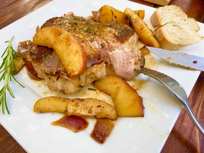 Cutting into pork chop on a plate with a fork and knife.