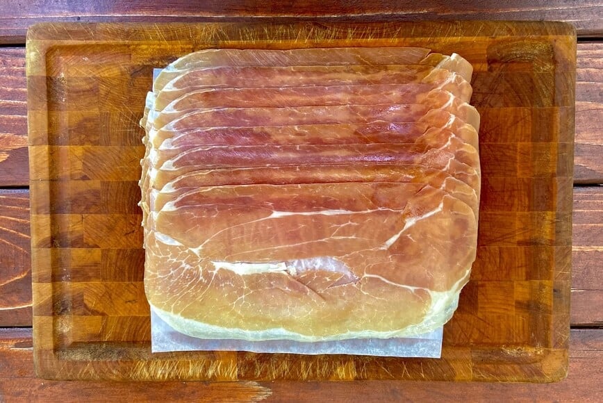 Prosciutto slices on a wooden cutting board.