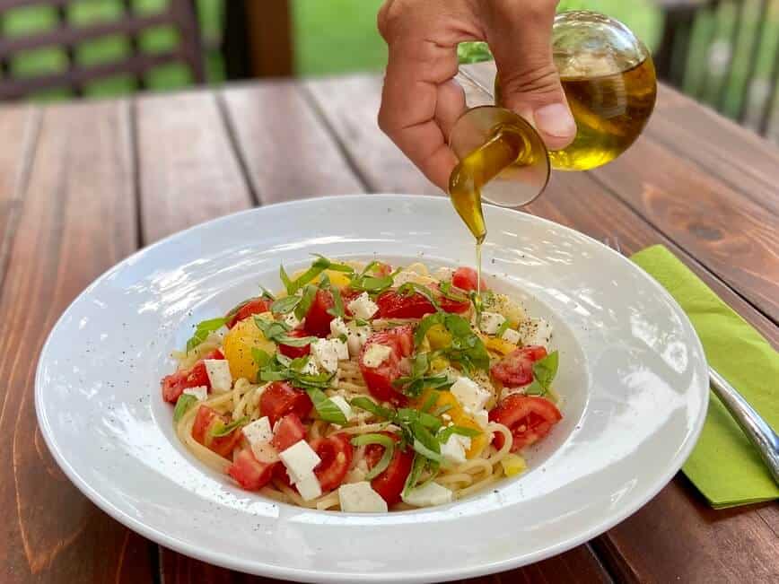 Pouring olive oil over finished pasta.