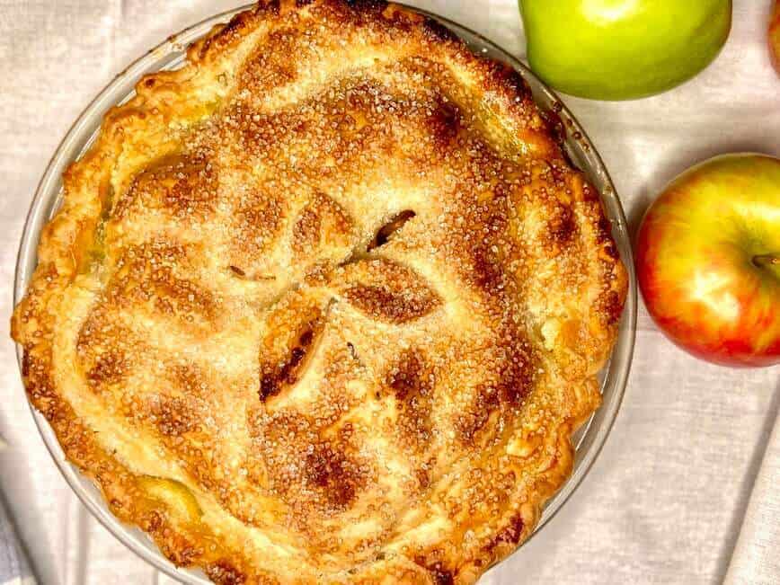 Whole apple pie on table, with apples.