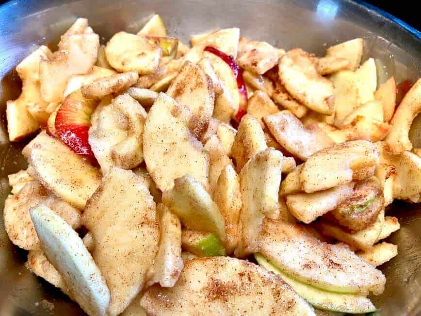 Sliced apples tossed with spices in bowl.