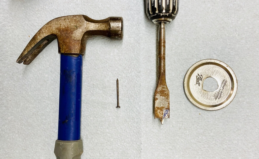 Hammer, nail, large drill bit, and lid with hole in the center.