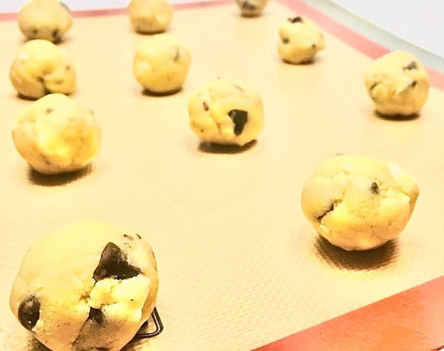 Cookie dough rolled into balls on a silicone mat lined baking sheet.