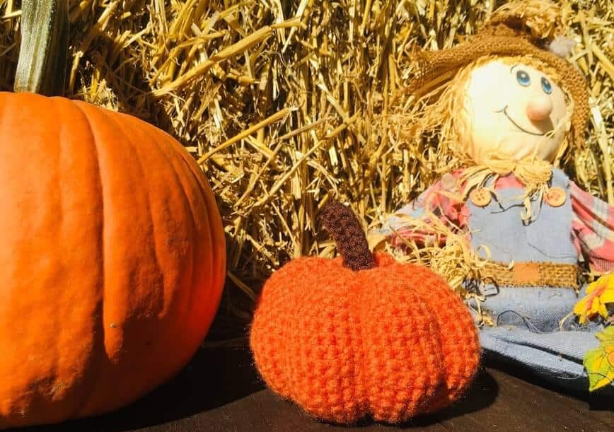 Crochet pumpkin with real pumpkin, hay, and scarecrow.