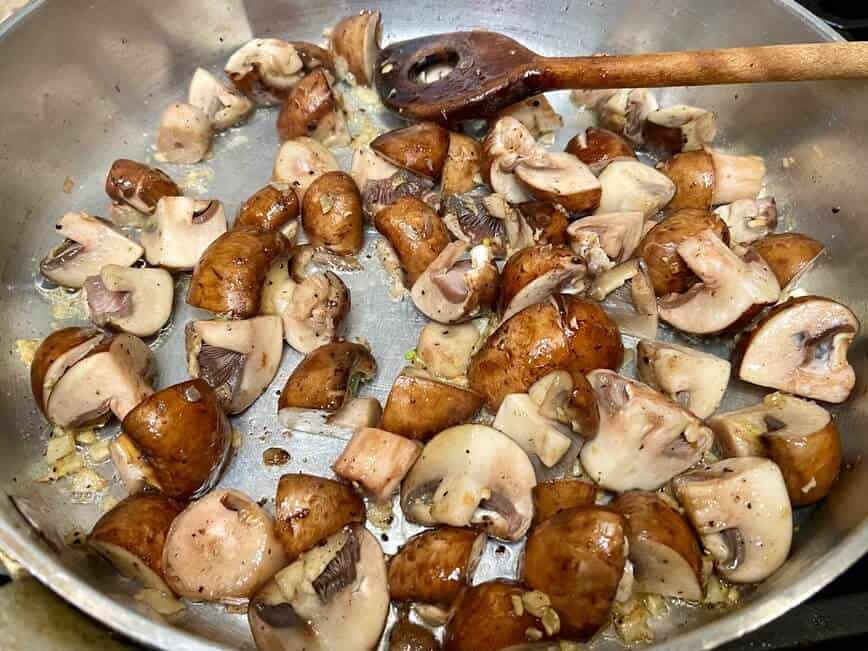 Sauteing mushrooms in a pan, stirring with a wooden spoon.