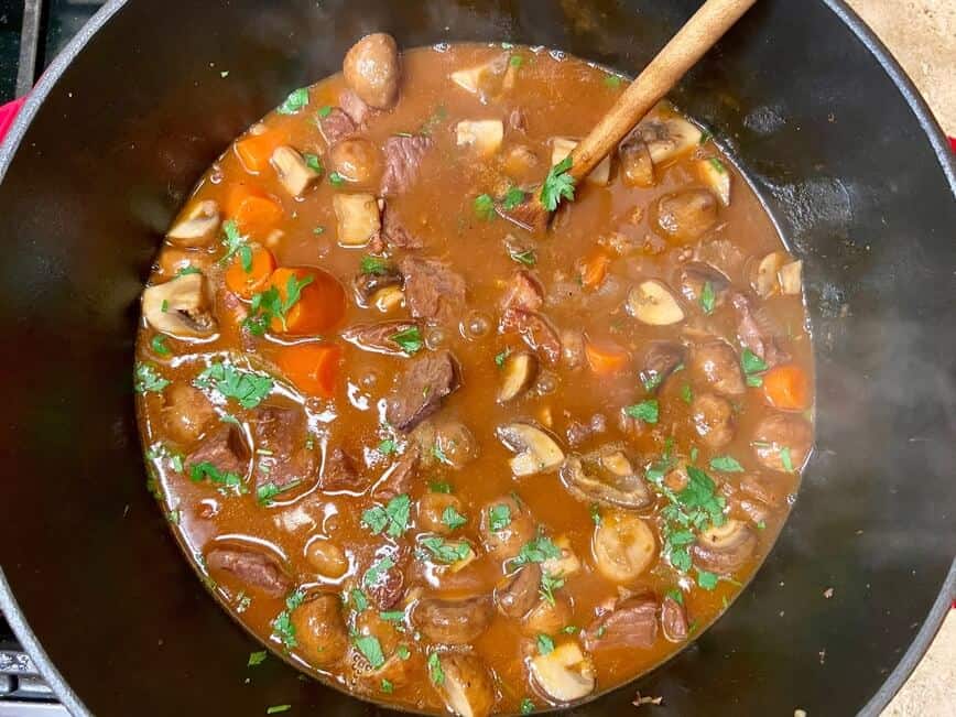 Stirring the beef bourguignon in a Dutch oven with a wooden spoon.