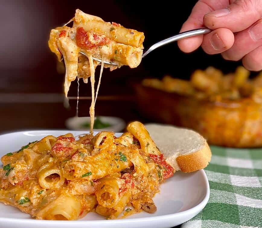Lifting some pasta on a fork, with strings of cheese from plate to fork.