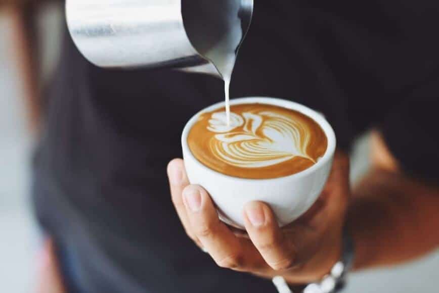 Coffee creamer being poured into a cup of coffee.