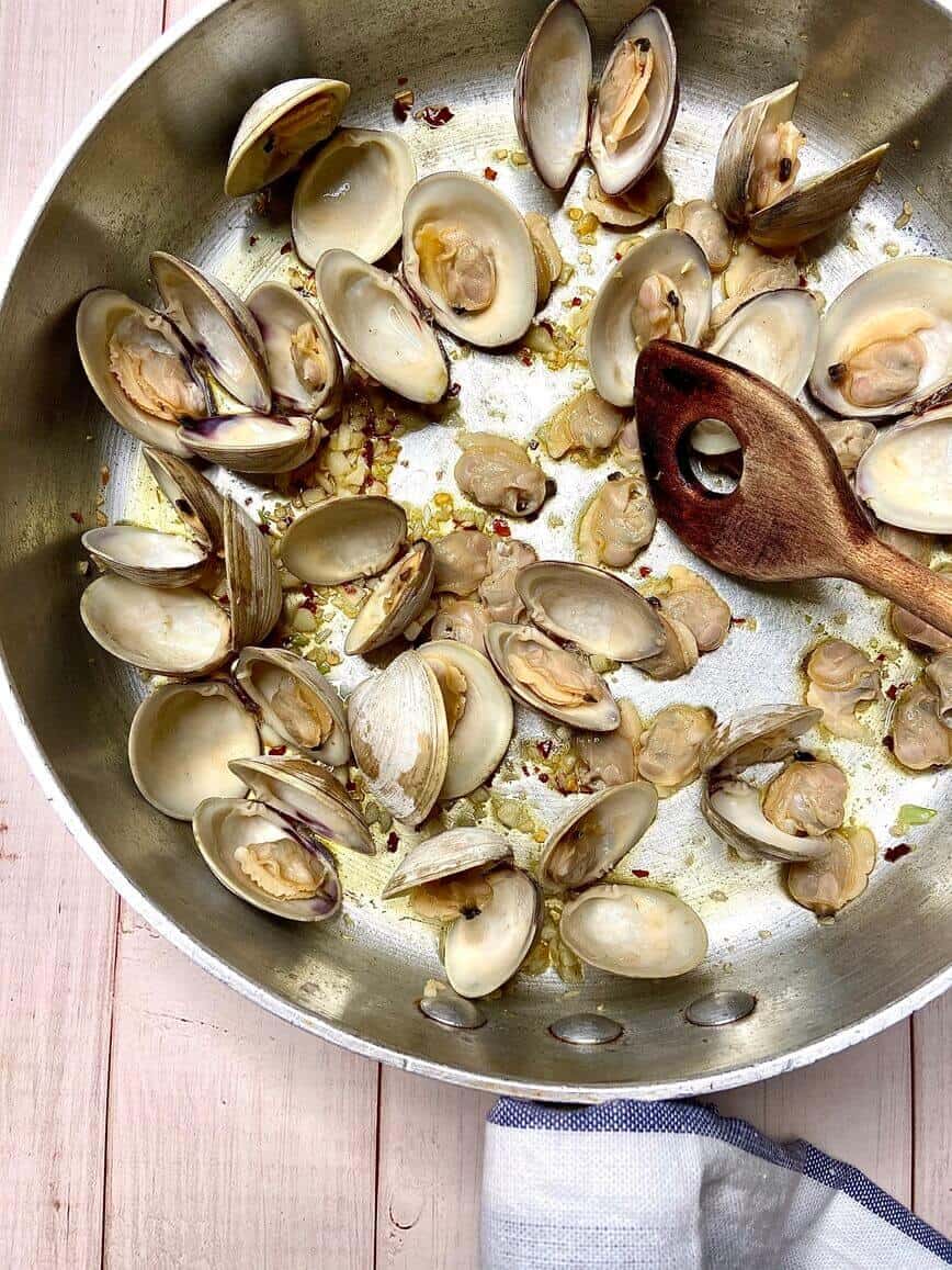 Stirring clams, garlic, and pepper flakes in a pot, with a wooden spoon.