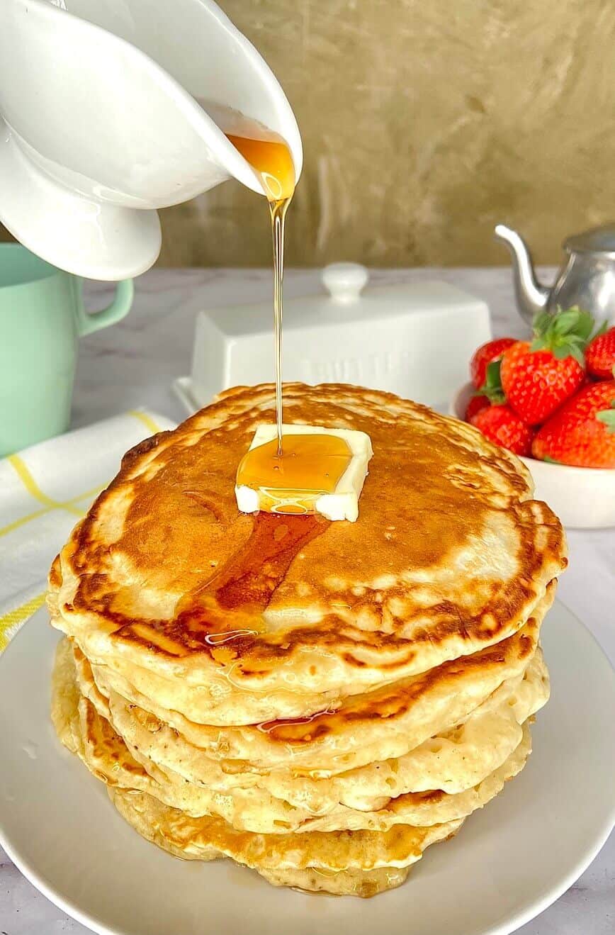 Pouring syrup over butter covered pancakes.