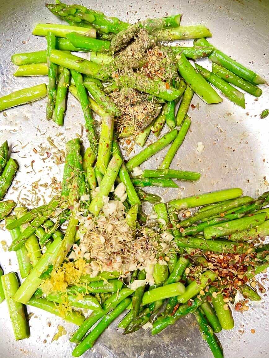 Cooking asparagus in a pan with herbs and spices.