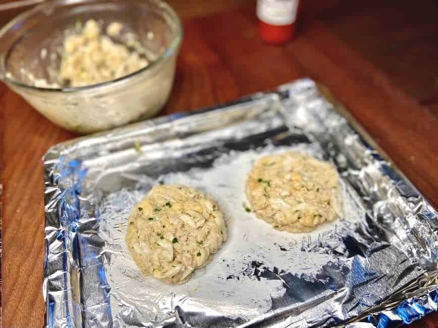 Two crab cakes on a foil lined pan greased with butter.