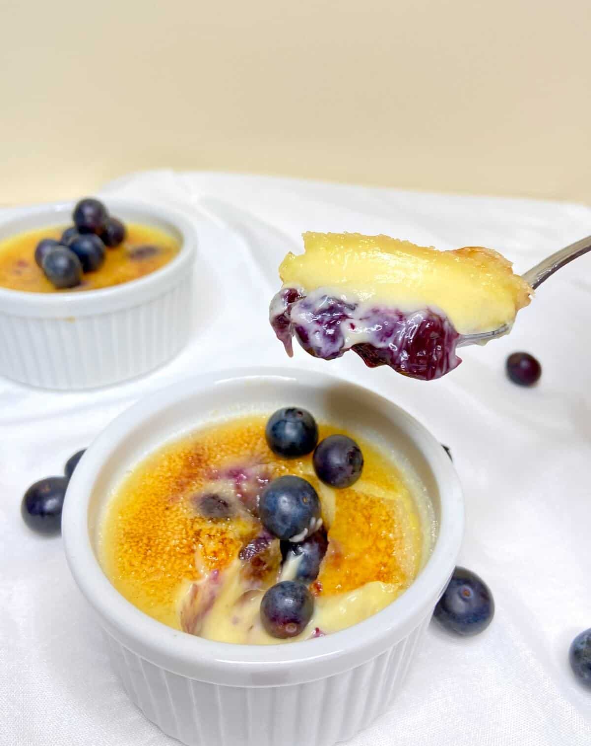 Blueberry creme brulee lifted on a spoon, over ramekin.