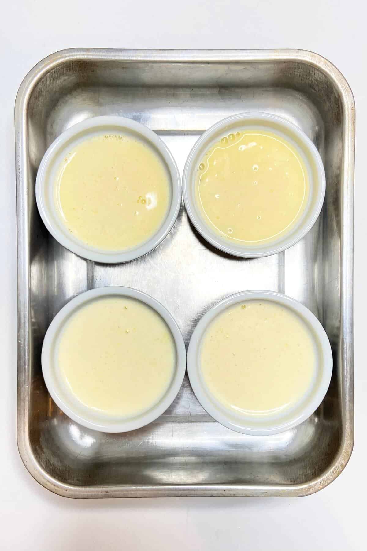 Four filled ramekins in a pan with water bath.