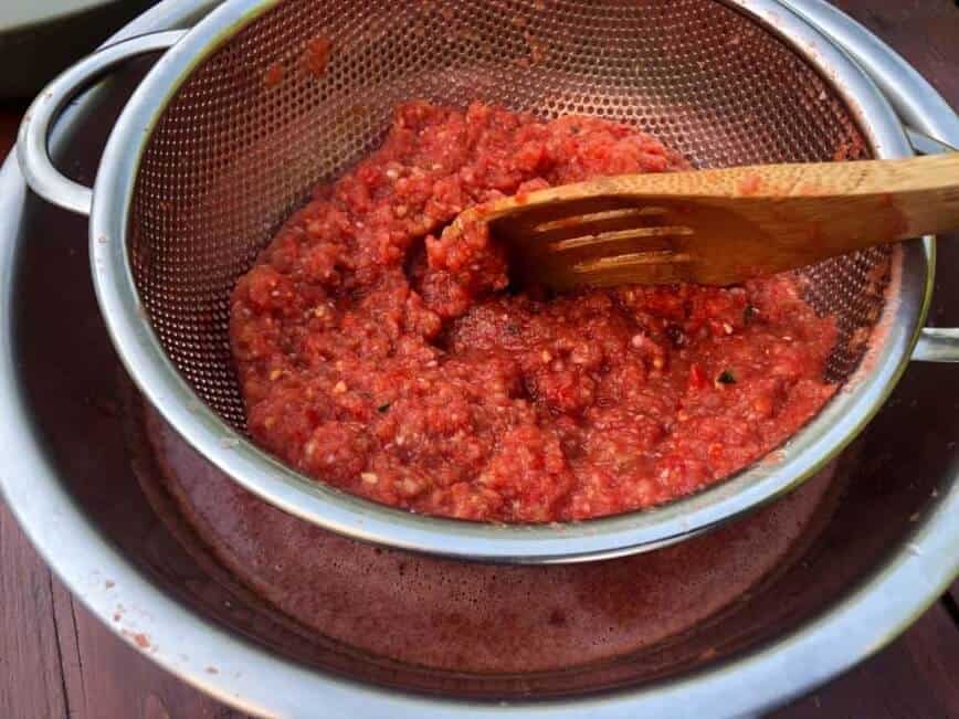 Pressing tomatoes through a mesh sieve with a wooden spoon.