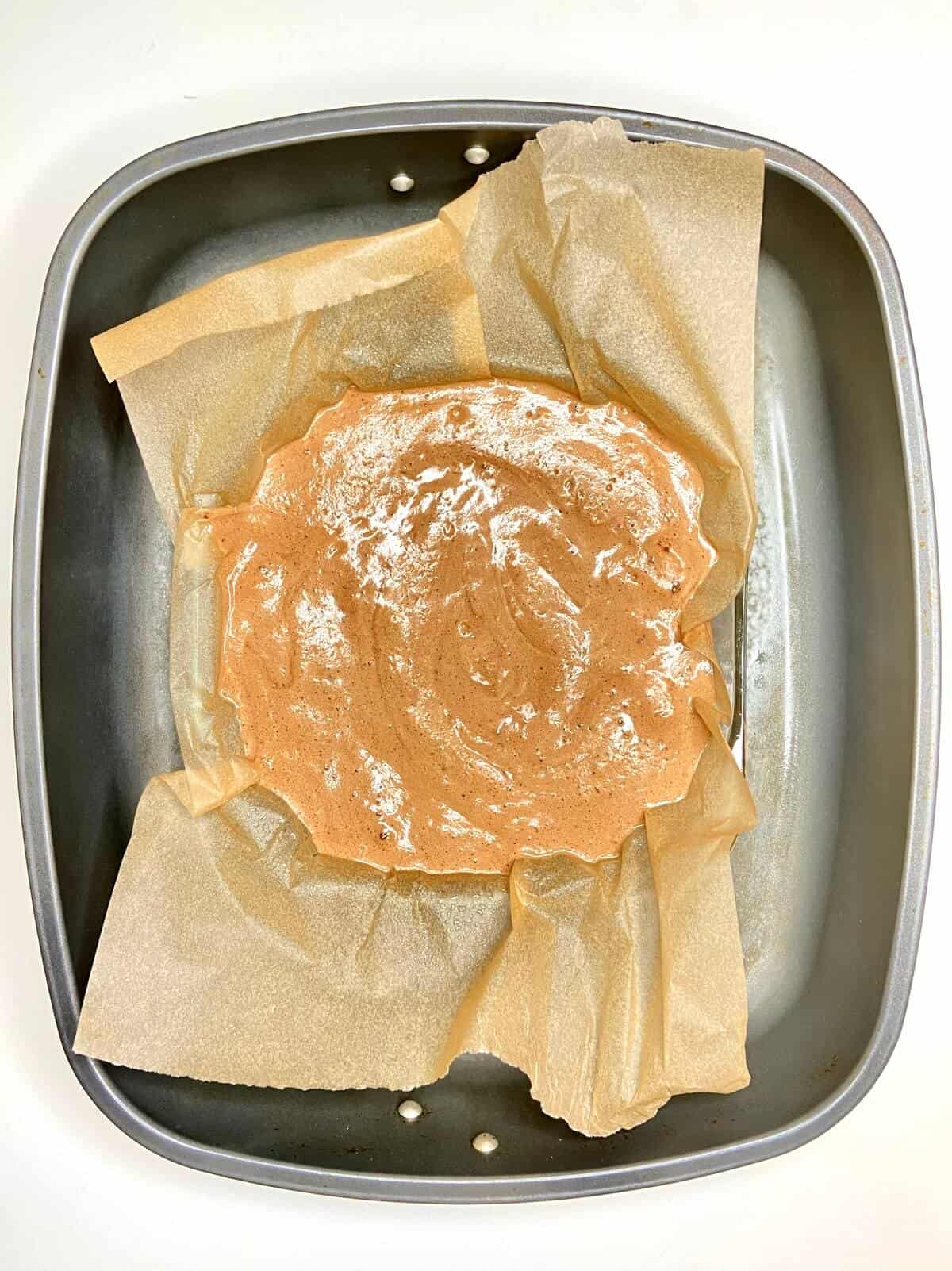 Batter poured into parchment lined baking dish, inside a larger pan for a water bath.