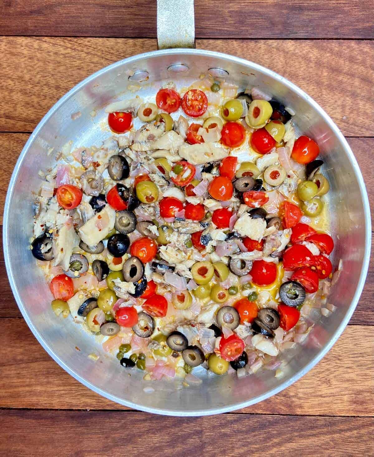 Cooking tomatoes, olives, capers, lemon juice, pepper flakes, and sardines.