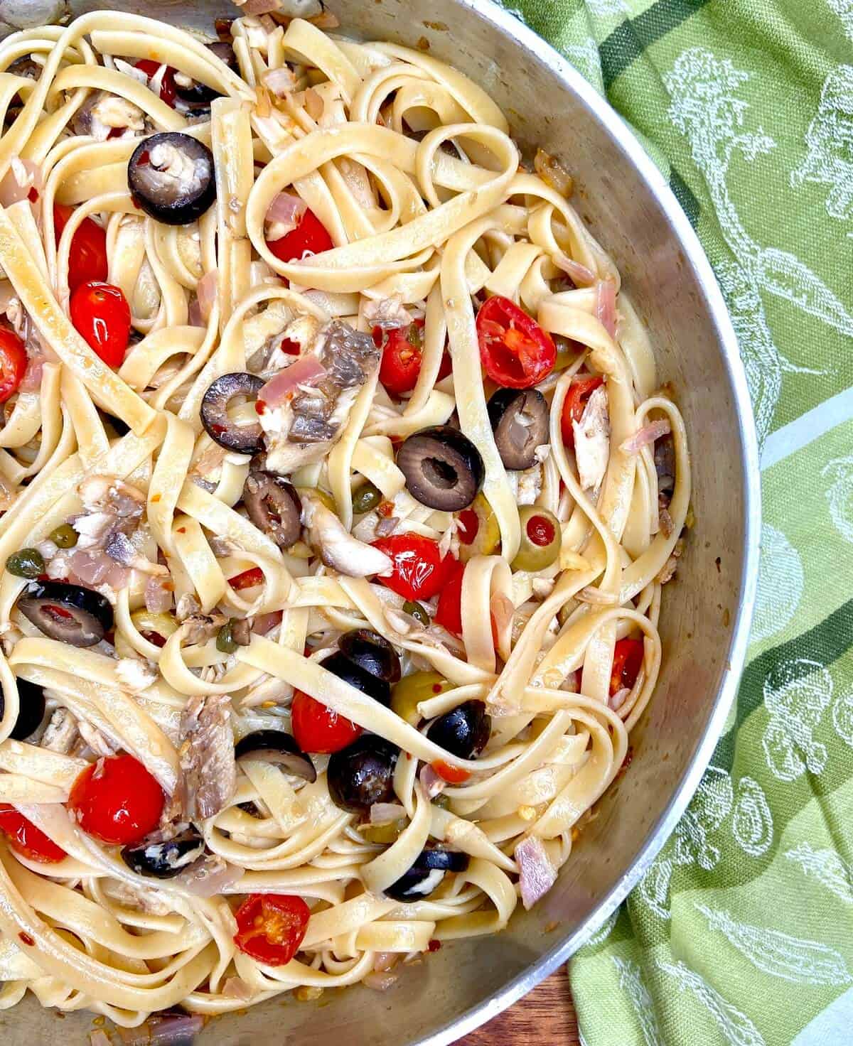 Mixed pasta, sardines, tomatoes, and olives in pan.
