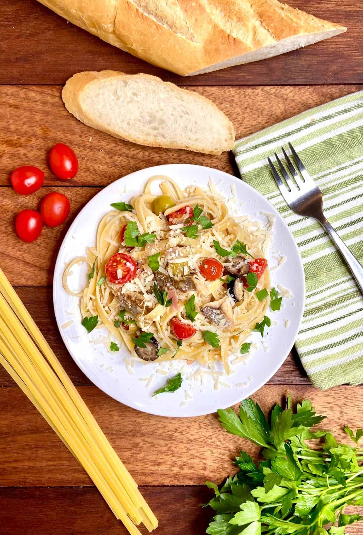 Pasta served on a plate, with slices of baguette and cherry tomatoes on a wood table.