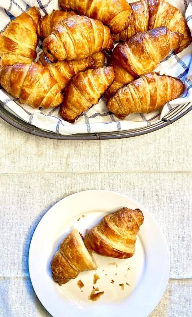 Bunch of croissants in a towel lined basket and one on a plate.