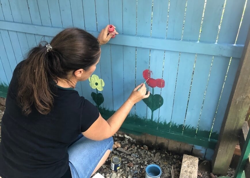 Viana painting happy little flowers along the bottom of the fence.