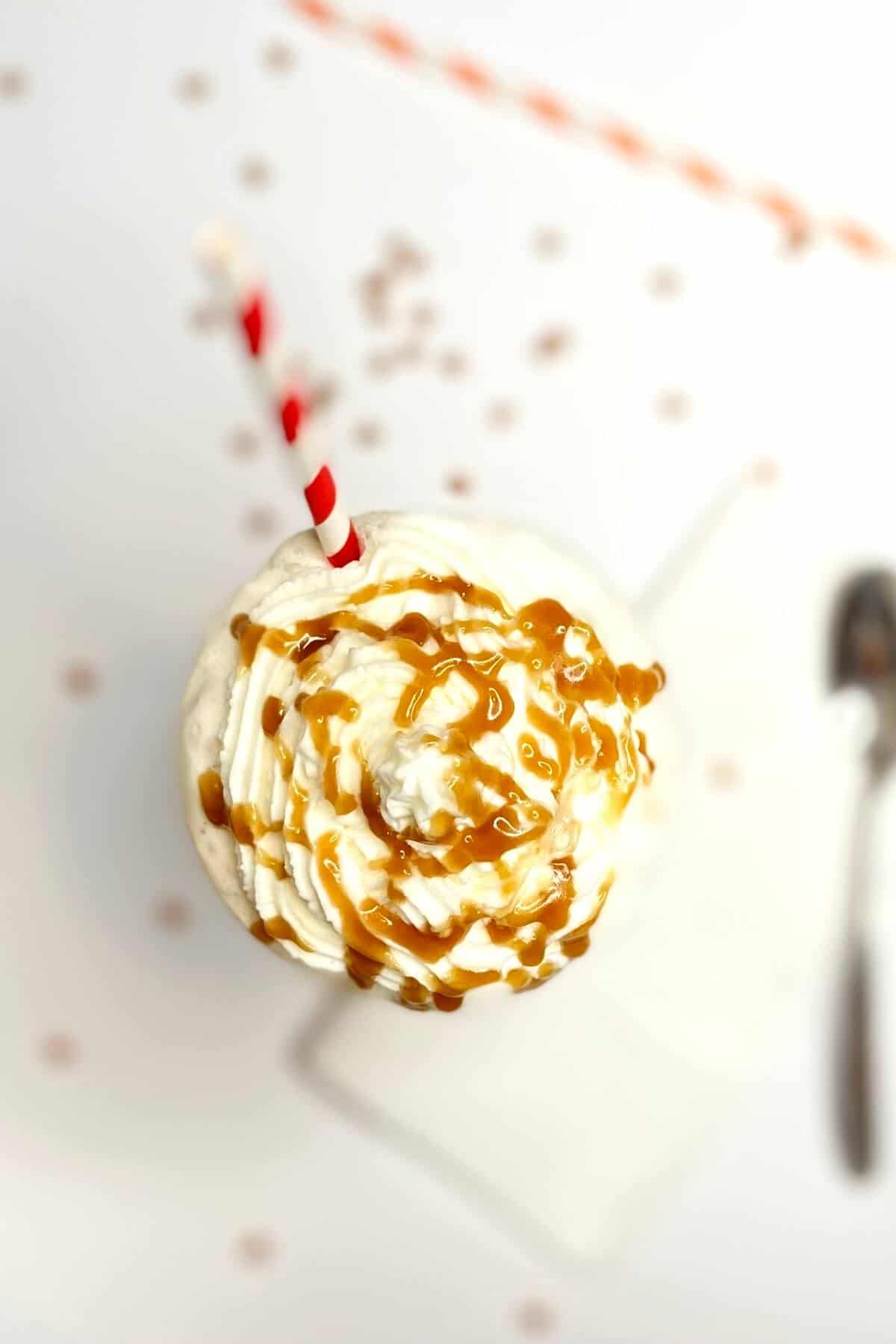 Top of milkshake, with caramel sauce drizzled on top and a red and white striped straw.