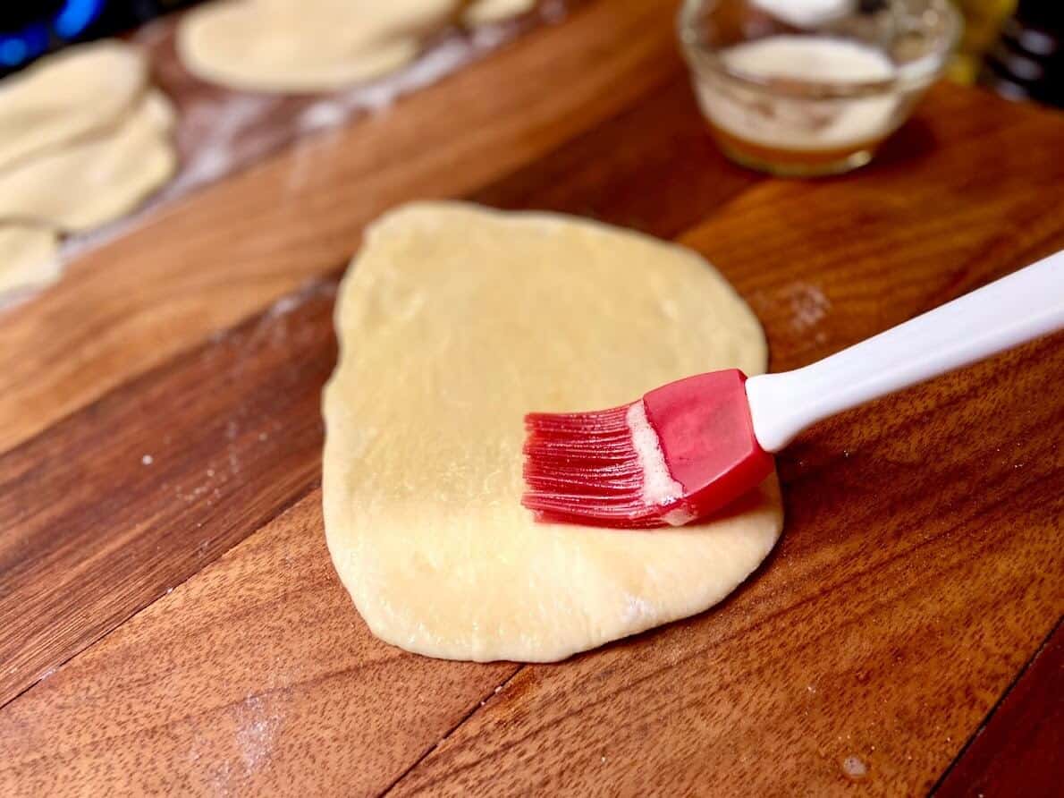 Silicone pastry brush, brushing rolled out naan dough with butter.