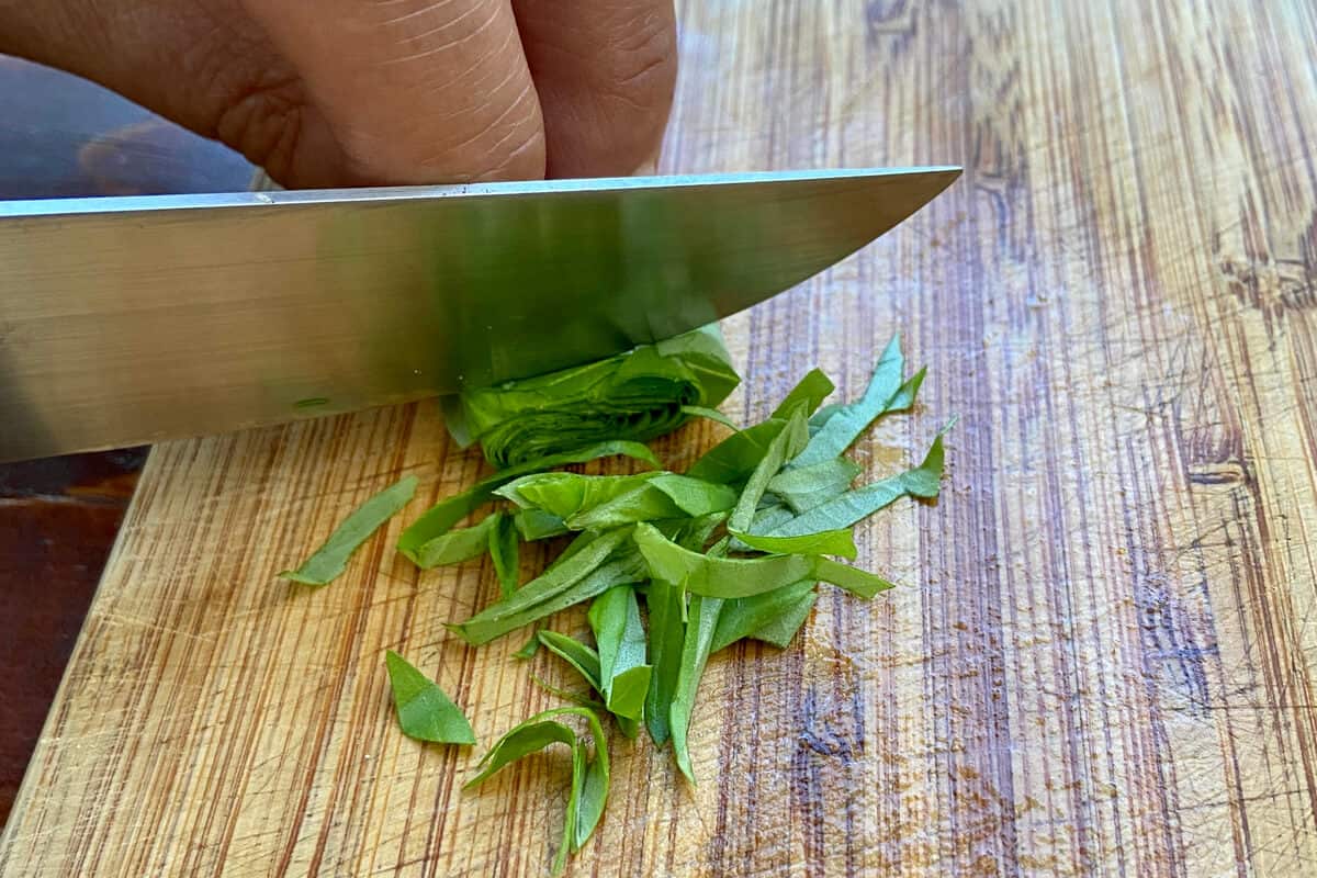 Knife cutting herbs on a cutting board.