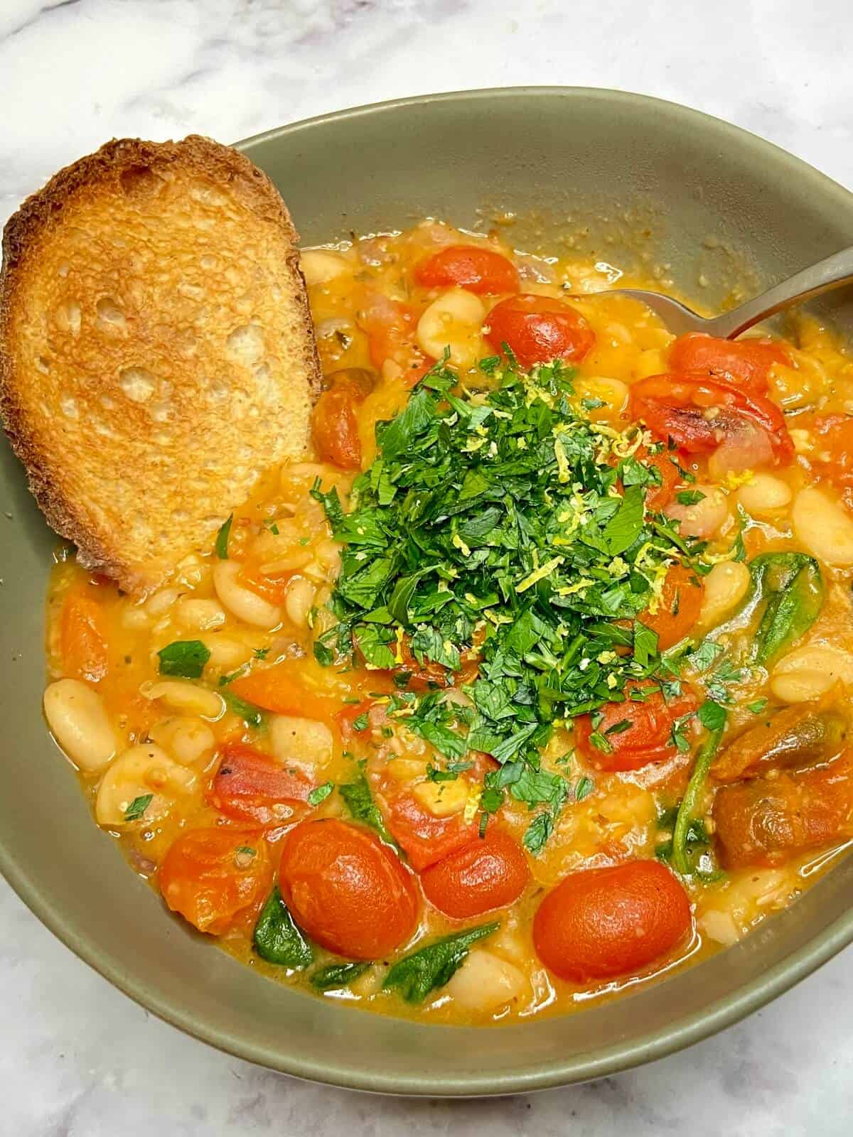 Stew served in a bowl with fresh chopped herbs and toasted baguette.