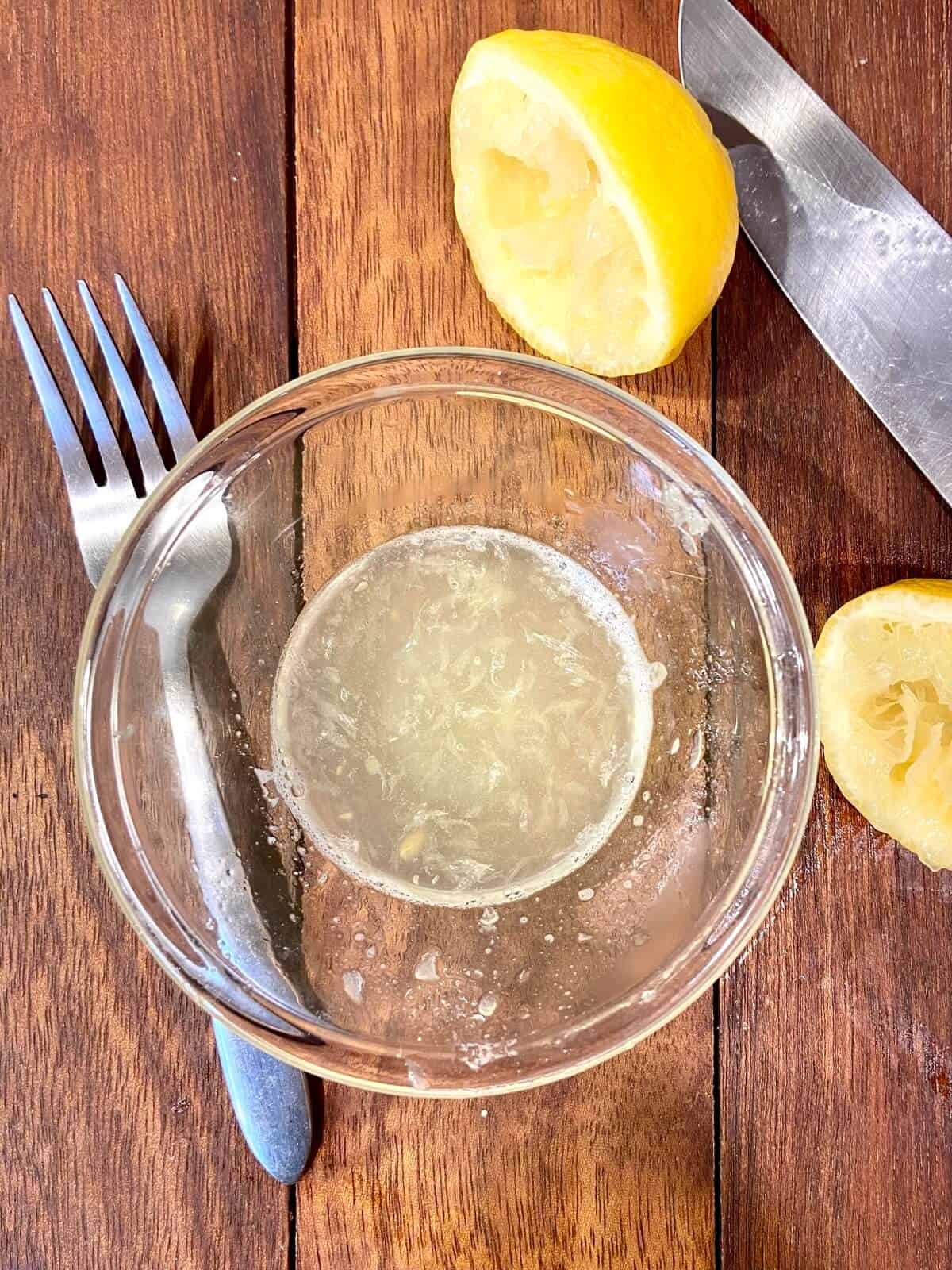 Lemon juice squeezed into a small bowl, with fork and knife on table.