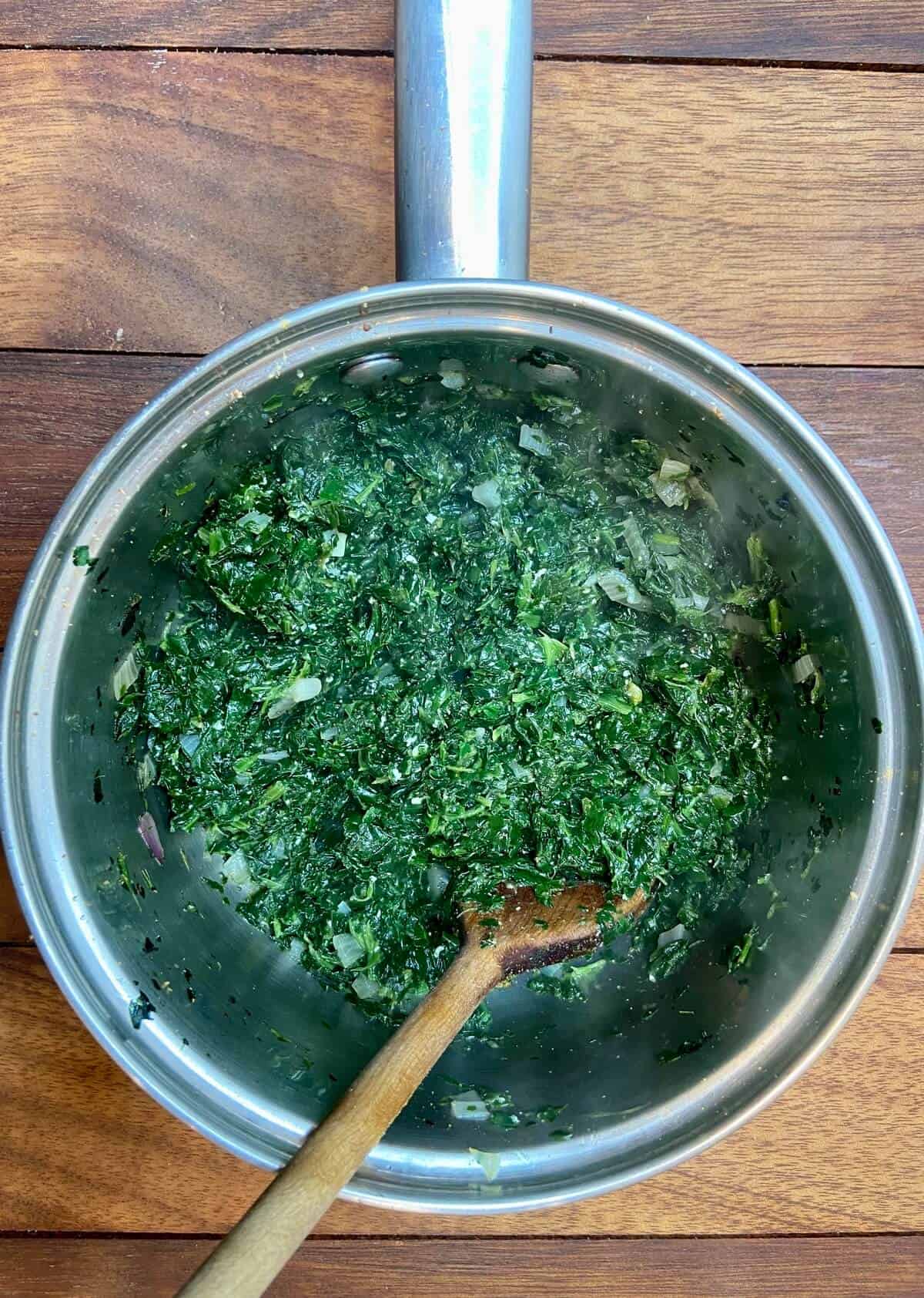 Spinach in a small pot, with a wooden spoon.