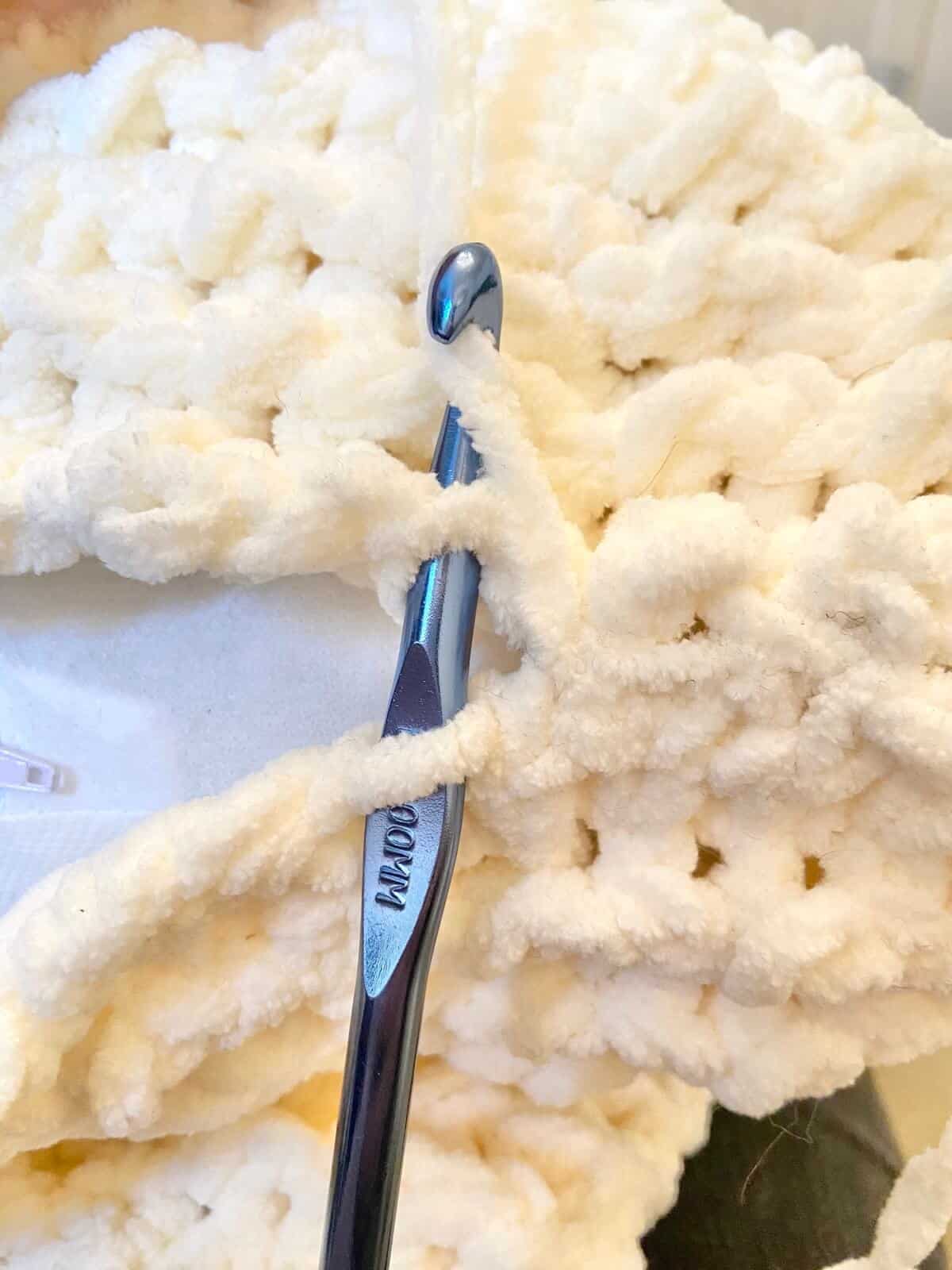Stitching two sides together with crochet hook and yarn.