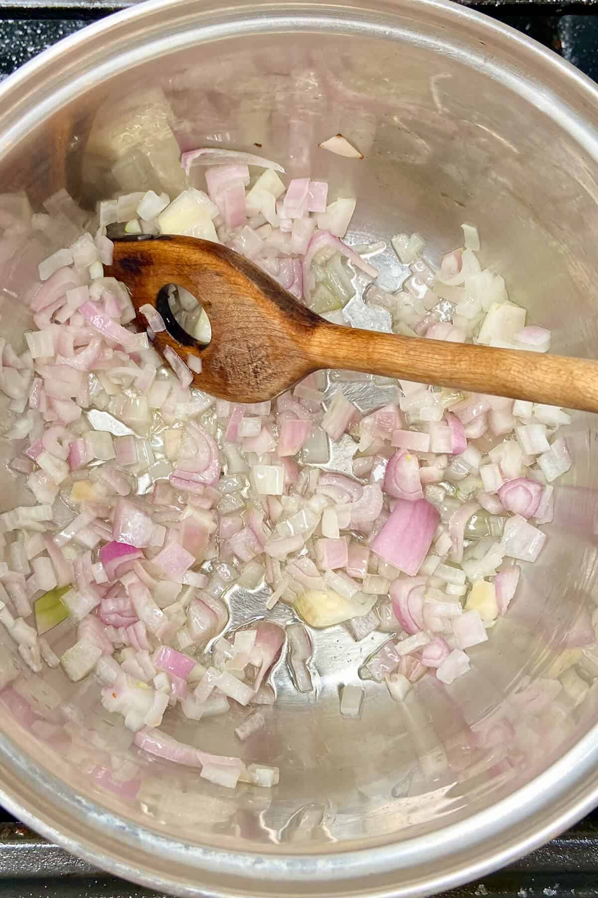 Stirring shallots in pot with a wooden spoon.