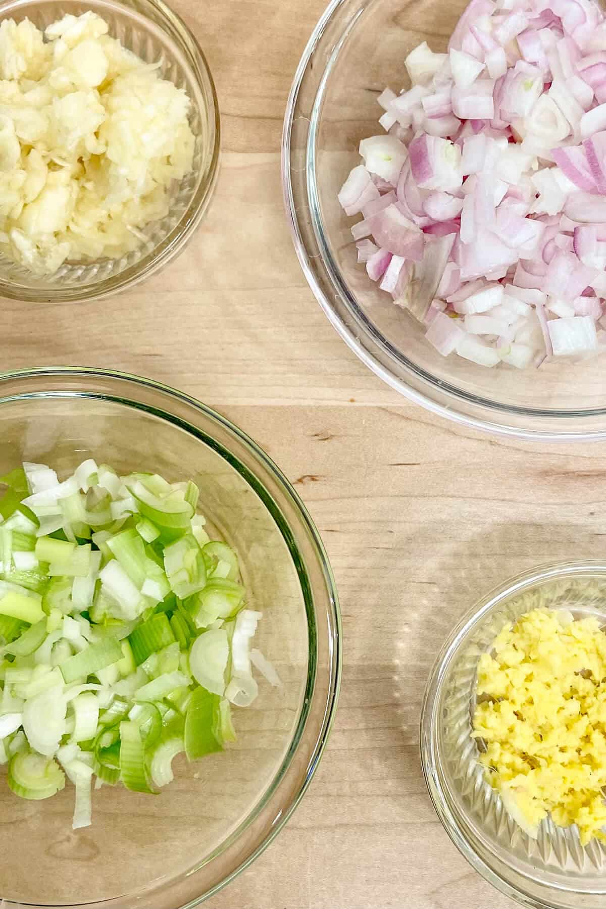 Scallions, garlic, ginger, and shallots in bowls mise en place.