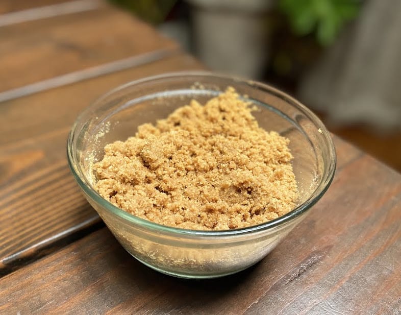 Crumbled graham crackers mixed with sugar and butter in a glass bowl.