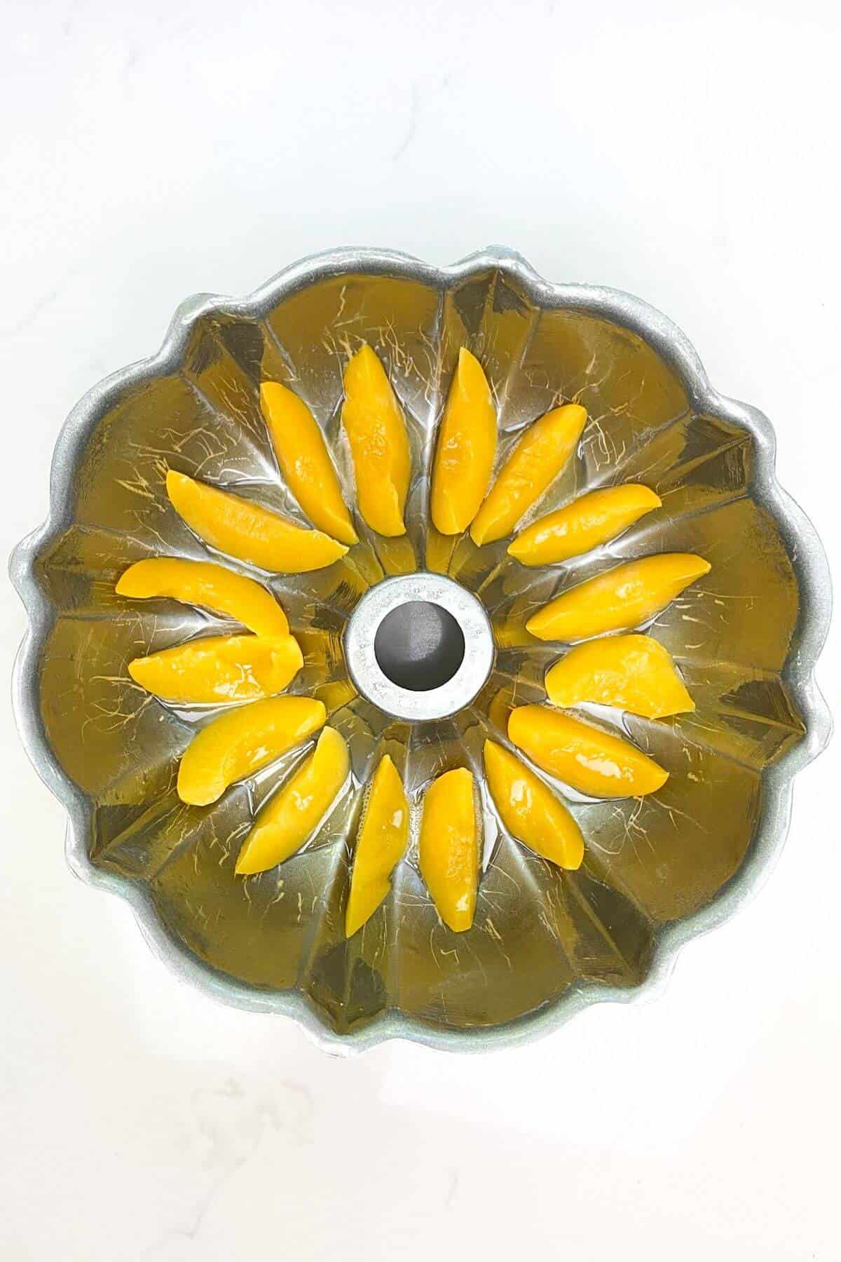 Sliced peaches lined along the bottom of a bundt pan.