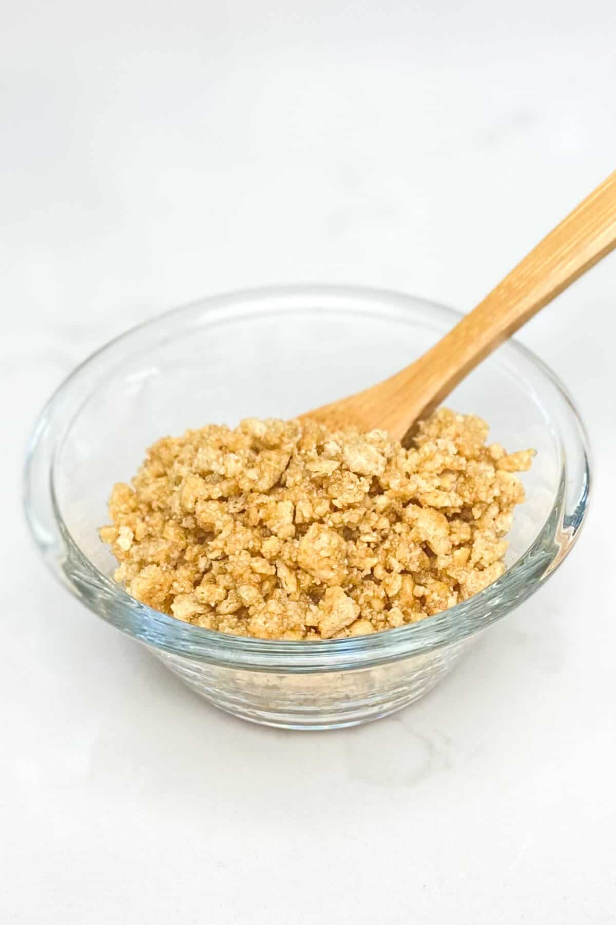 Graham cracker crumbs mixed with butter in a small glass bowl