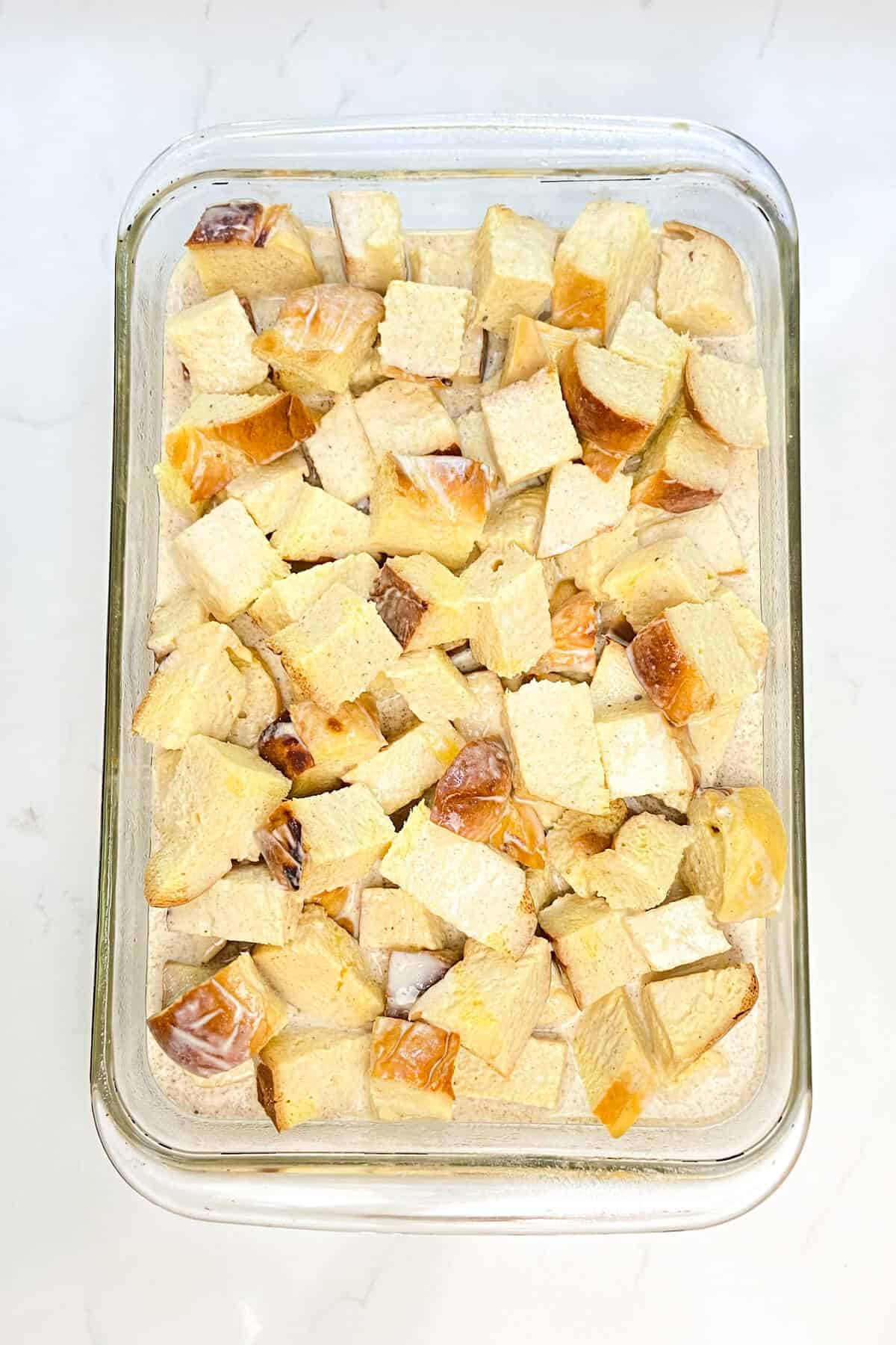 Cubed bread with milk mixture in pan.