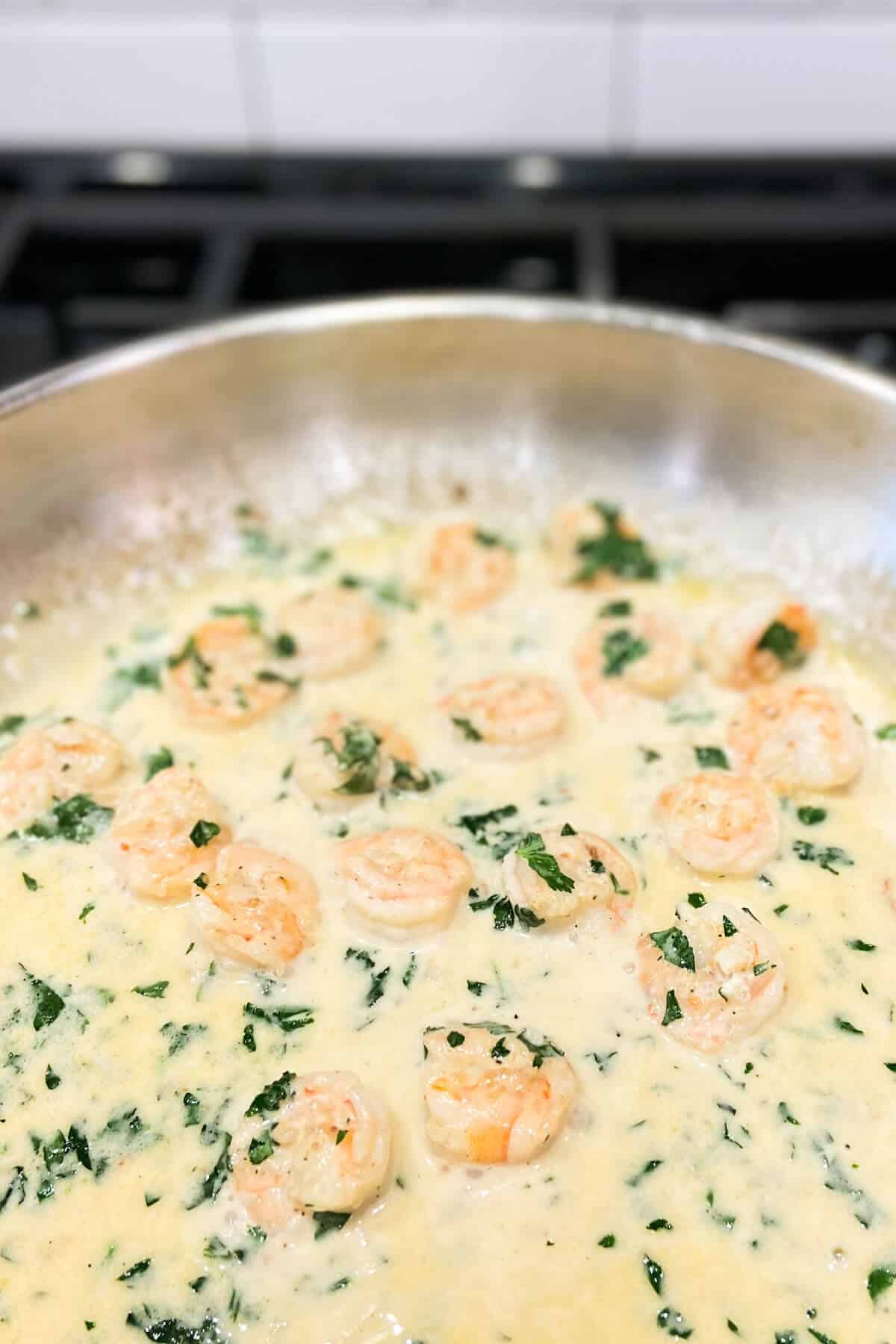 Shrimp cooking in cream sauce with parsley.
