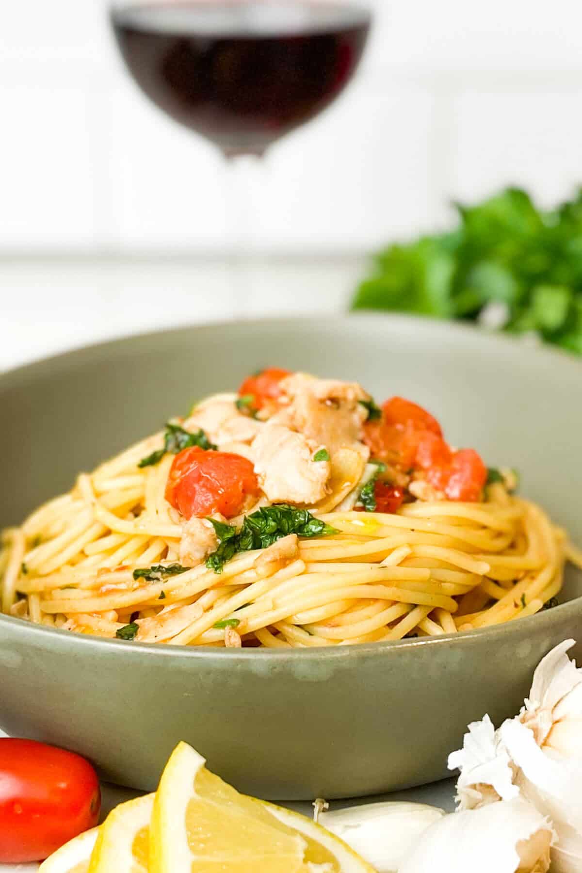 Bowl of pasta, with lemon slices, tomatoes, and parsley on table.