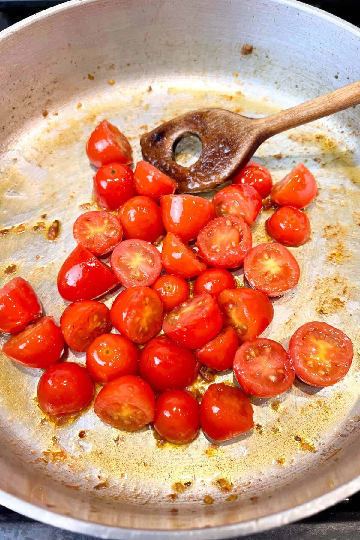 Stirring tomatoes in pan with wooden spoon.