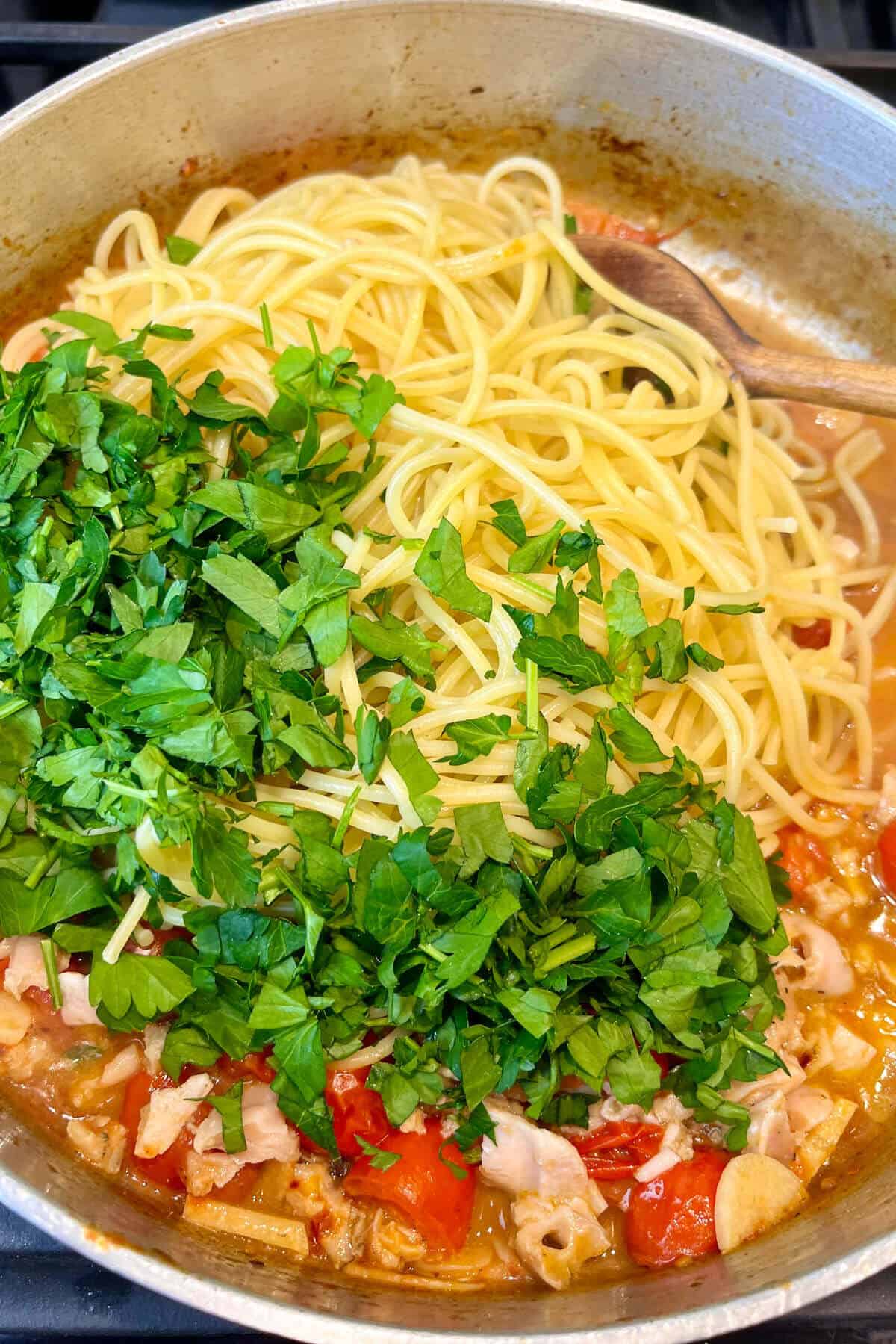 Tossing spaghetti and parsley in sauce.