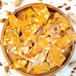 Quick & easy nut brittle, broken into pieces, on a round wooden board.